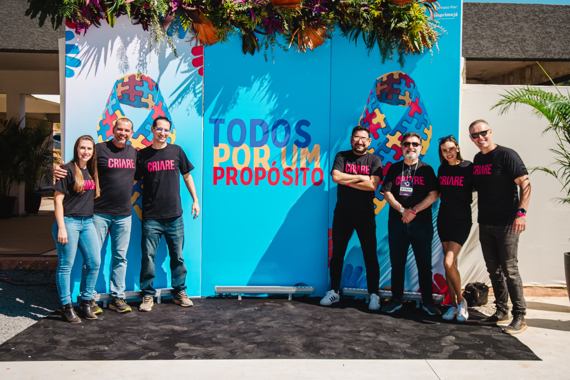 Equipe organizadora reunida em frente ao painel Todos por um Propósito