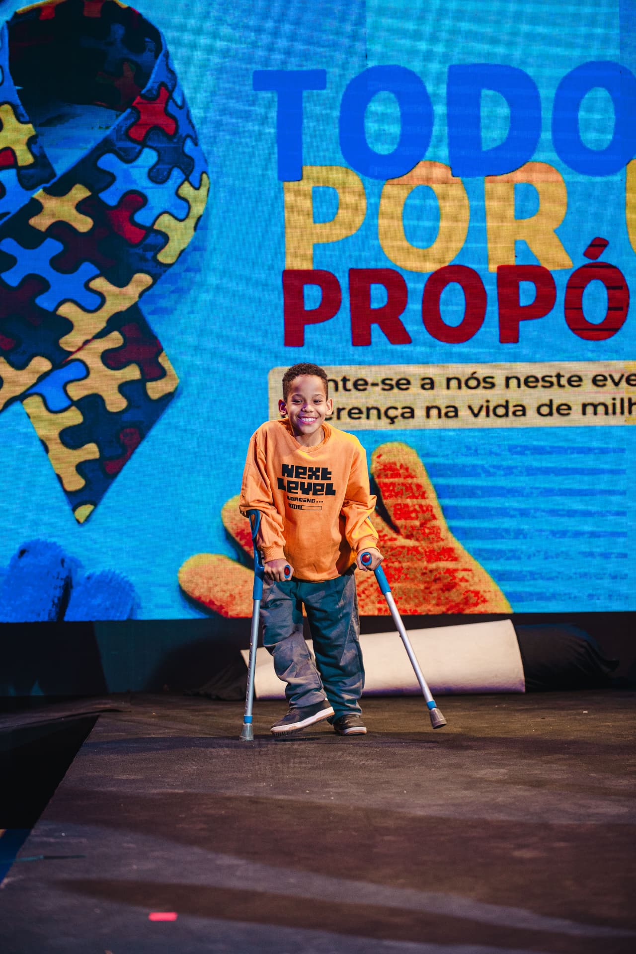 Criança sorrindo na passarela em frente ao painel Todos por um Propósito